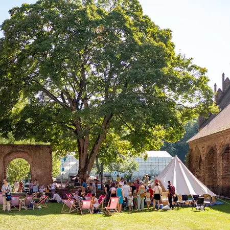 Das Bild zeigt den Klosterhof mit Menschen, die stehen und sitzen und einem großen Zelt.