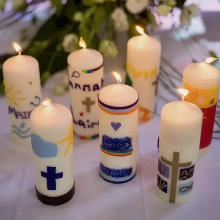 Mehrere individuell gestaltete Konfirmationskerzen sind zu sehen. Sie sind angezündet und stehen auf einem Altar. Im Hintergrund Blumen.